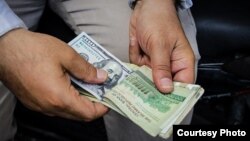 An Iranian man holds a stack of U.S. and Iranian bank notes. The Bonbast.com website, which tracks Iran’s unofficial exchange rates, showed the rial at a record low of 160,000 to the dollar on Sept. 24, 2018. (Photo Courtesy of Tasnim news agency)