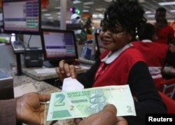 A till operator poses with new bond notes at a supermarket in Harare, Nov. 28, 2016.