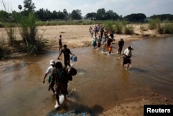 FILE - A group of Myanmar refugees, who crossed over from Myanmar to Thailand when a battle erupted between Myanmar's soldiers and rebels, walk across a stream of water at the Thai border town of Mae Sot, Nov. 8, 2010.