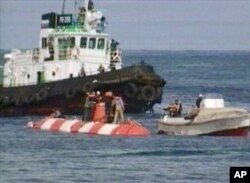 Crew members of a Russian minisubmarine and rescue team members stand on its hull (white and red streaks) shortly after the sub surfaced in the Beryozovaya Bay about 15 kilometers (10 miles) off the Kamchatka coast, Aug. 7, 2005, in this image taken from television. The minisub, trapped for nearly three days under the Pacific Ocean, surfaced with all seven people aboard alive after a British remote-controlled vehicle cut away the undersea cables that had snarled it.