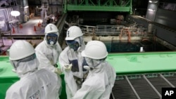 Сотрудники Tokyo Electric Power Co. (TEPCO) и журналисты в защитных костюмах смотрят в бассейн с топливными стержнями в здании четвертого реактора на АЭС «Фукусима». Префектура Фукусима. Япония. 7 ноября 2013 г.