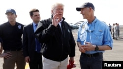U.S. President Donald Trump stands with FEMA Administrator Brock Long (L) and U.S. Rep Ron DeSantis (R-FL) as he talks to Florida Governor Rick Scott (R) after the president arrived to tour storm damage from Hurricane Michael at Eglin Air Force Base, Flo