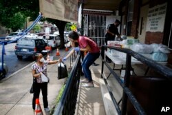 In this June 11, 2020, photo Lourdes Sherby, center, with Guadalupe Family Services, hands diapers to Louisa Peralta in Camden, N.J. “I think we’re received a lot better than we used to be,” said Sgt. Dekel Levy, 41, as he helped hand out diapers.