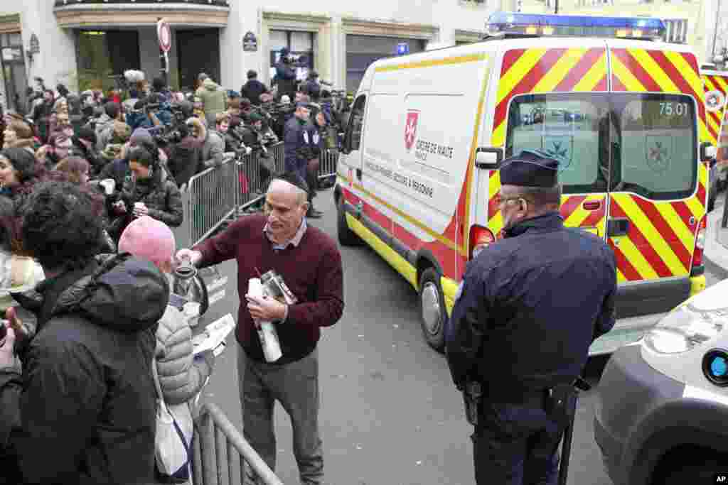 A local resident distributes coffee to reporters gathered at the scene after terrorists stormed a French paper, killing at least 12 people, in Paris, Jan. 7, 2015.