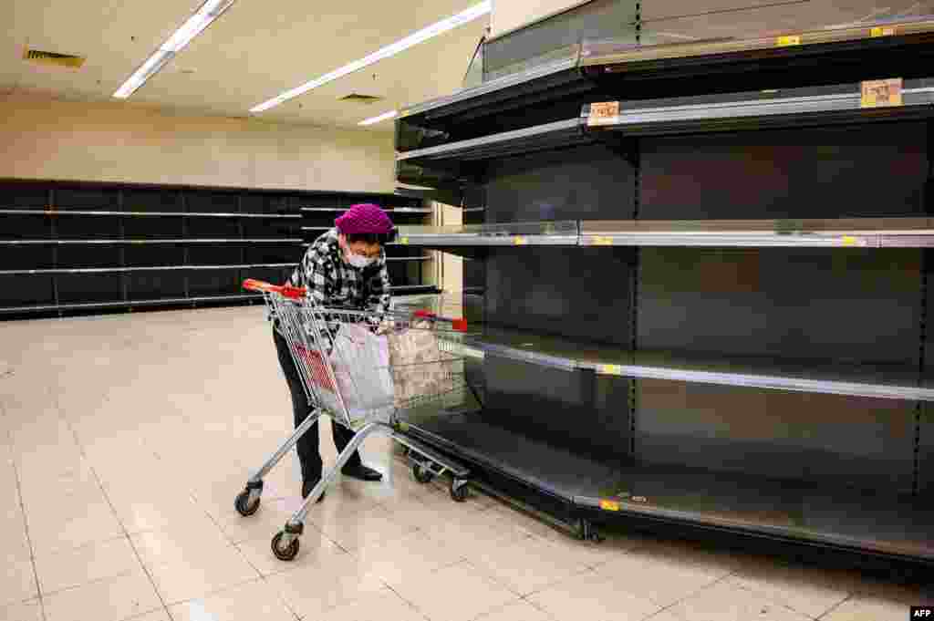 A shopper wearing a protective face mask sorts items in her shopping cart as she stands next to bare supermarket shelves in Hong Kong.