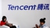 FILE - Visitors use their smartphones underneath the logo of Tencent at the Global Mobile Internet Conference in Beijing, May 6, 2014. 