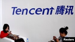 FILE - Visitors use their smartphones underneath the logo of Tencent at the Global Mobile Internet Conference in Beijing, May 6, 2014. 