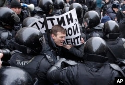 FILE - Riot police officers detain a protester holding a poster reading 'Putin, you are not my President' during a rally in St. Petersburg, Russia, Jan. 28, 2018.