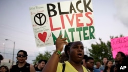 ນາງ Desiree Griffiths ຖືປ້າຍກ່າວວ່າ "Black Lives Matter" ພ້ອມດ້ວຍຊື່ຂອງທ້າວ Michael Brown ແລະ Eric Garner ຜູ້ຊາຍຜິວດຳ ທີ່ຖືກຕຳຫລວດຍິງຕາຍ. 
