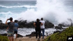 Onlookers watch large waves crash on the rocks at Wawamalu Beach, Aug. 24, 2018, in Waimanalo, Hawaii.