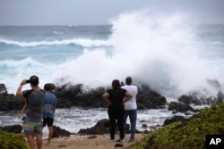 Onlookers watch large waves crash on the rocks at Wawamalu Beach, Aug. 24, 2018, in Waimanalo, Hawaii.