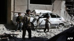 Anak-anak di Suriah berjalan di antara puing-puing di daerah Dourna yang dikuasai pemberontak, di sebelah timur Damaskus, menyusul serangan udara oleh pasukan rezim pemerintah (13/3). (AFP/Abd Doumany)