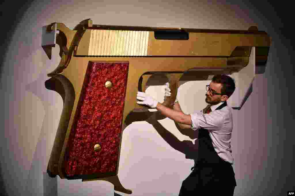 An employee poses with an enlarged model gun entitled &quot;James Bond&#39;s New Gun,&quot; designed by David Collins and Floris Van Den Broecke for Granda Publishing LTD., 1977, at Sotheby&#39;s auction house in London.