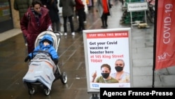 FILE - A woman, pushing a child in a stroller, walks past signage outside a pop-up vaccination site for COVID-19 vaccine and booster shots, in Hammersmith and Fulham, in Greater London, Britain, Dec. 3, 2021.