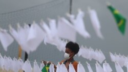 Seorang anggota LSM Rio de Paz menaruh sapu tangan berwarna putih sebagai simbol perpisahan terhadap 600.000 korban meninggal akibat COVID-19 di Brazil, di Pantai Copacabana, Rio de Janeiro, pada 8 Oktober 2021. (Foto: Reuters/Pilar Olivares)