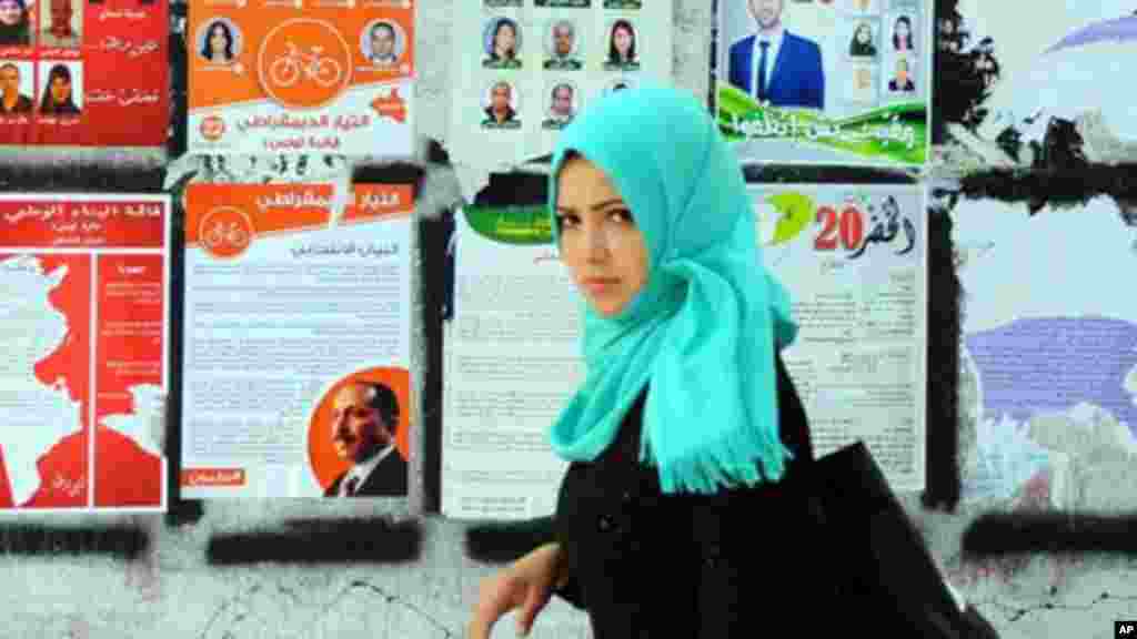 Une femme marche à côté des affiches de la campagne électorale pour les prochaines élections législatives à Tunis, en Tunisie, le jeudi 23 octobre 2014. 