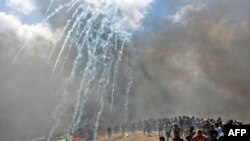 Palestinians run for cover from tear gas fired by Israeli forces near the border between the Gaza strip and Israel east of Gaza City, May 14, 2018, as Palestinians protest over the inauguration of the US embassy following its controversial move to Jerusal