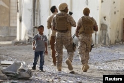 FILE - A boy walks past soldiers from the Saudi-led coalition patrolling a street in Yemen's southern port city of Aden, Sept. 26, 2015.