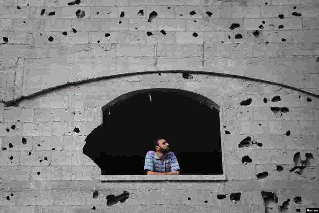 A Palestinian man looks through a window scarred with shrapnel from a neighbouring building that police said was hit by an overnight Israeli air strike, in Jabaliya in the northern Gaza Strip, July 24, 2014.
