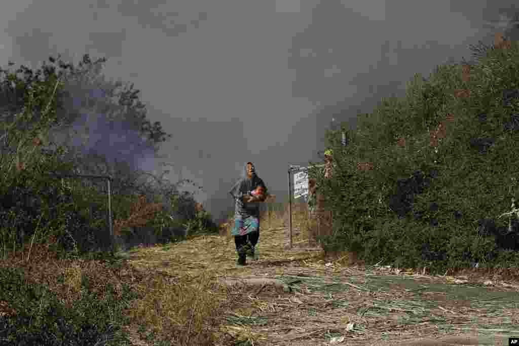 A migrant holds her baby as she runs from a small fire in a field near Mytilene town, on the northeastern island of Lesbos, Greece, Sept. 12, 2020.