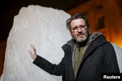 FILE - Olafur Eliasson, a Danish-Icelandic artist, poses in front of a block of ice that was havested in Greenland and transported in a refrigerated container for a project called "Ice Watch Paris," in Paris, France, Dec. 3, 2015