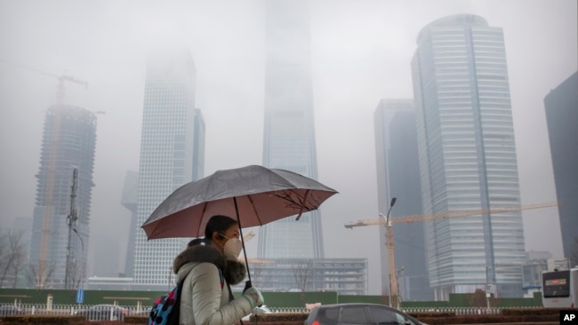 A woman wears a face mask as she walks along a street in the central business district in Beijing, Saturday, Feb. 29, 2020. (AP Photo/Mark Schiefelbein)