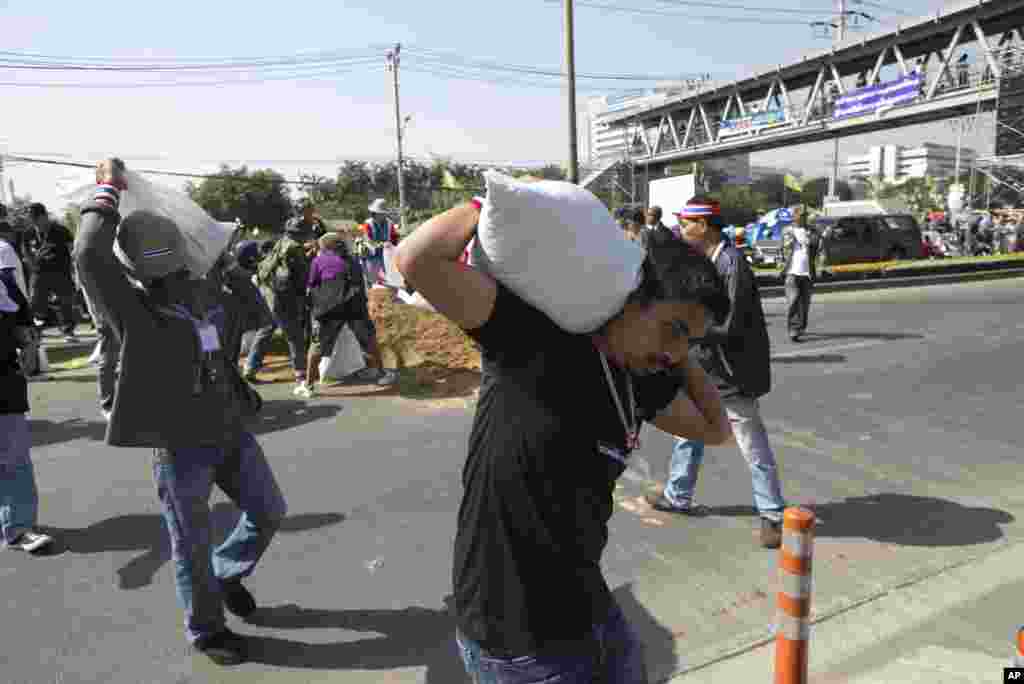 Anti-government protesters carry sand bags to set up road blocks during a rally outside the government complex in Bangkok, Jan. 13, 2014. 