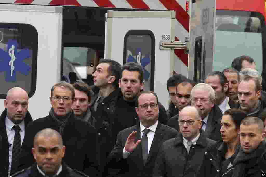 French President Francois Hollande, center, flanked with security forces gestures, as he arrives outside the French satirical newspaper Charlie Hebdo's office, in Paris, Jan. 7, 2015. 