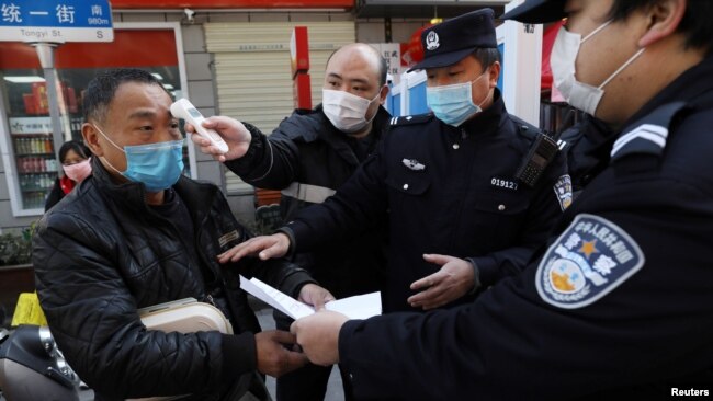 中国武汉一个街口设立的检疫站社区工作人员给一名男子测量体温,同时警察检查男子的证件。(2020年2月20日)