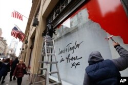 Workers scrape a sign off a display window outside Lord & Taylor's flagship Fifth Avenue store after it closed for good mid-afternoon, Jan. 2, 2019, in New York.