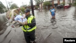 Un policía ayuda a evacuar un bebé de 21 meses, seguido por su madre en Slidell, Luisiana.