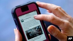 In this April 28, 2015, file photo, an Associated Press staffer poses using a mobile phone to read the news from The Huffington Post on Facebook, in Los Angeles. (AP Photo/Richard Vogel, File)