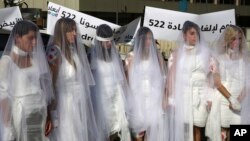 FILE - Lebanese women, dressed as brides in white wedding dresses stained with fake blood and bandaging their eyes, knees and hands stand in front of the government building in downtown Beirut, Lebanon, Dec. 6, 2016. 