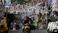 Seorang warga Filipina mengendarai motornya melewati poster-poster kampanye yang menghias jalanan menjelang Pemilu Sela di wilayah suburban kota Quezon, sebelah utara Manila, Filipina (12/5).