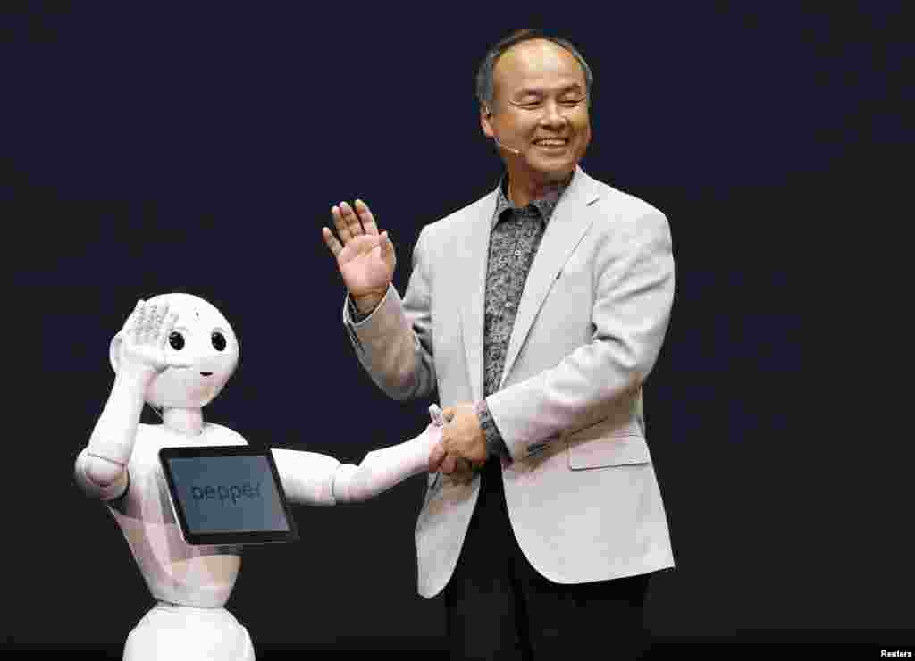 SoftBank Corp. Chief Executive Masayoshi Son waves with the company&#39;s human-like robots named &#39;Pepper&#39; in Tokyo, Japan.&nbsp;&nbsp; SoftBank Corp is developing human-like robots which will be used to staff its cellphone stores.