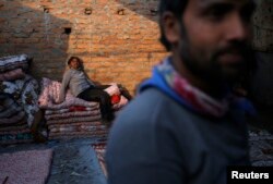 FILE - A migrant worker from India sits in the sun as he takes a break while making blankets from recycled cotton in Kathmandu, Nepal Dec. 22, 2015.