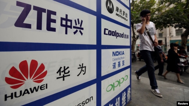 一名中国男子从武汉街头有着华为和中兴标徽的广告牌前走过。（资料照片）