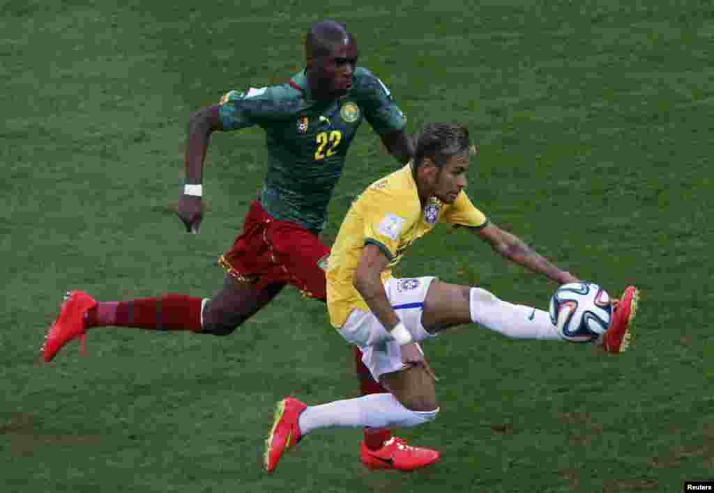 Brazil's Neymar, right, controls the ball in front of Cameroon's Allan Nyom during their match at the Brasilia national stadium in Brasilia, June 23, 2014.
