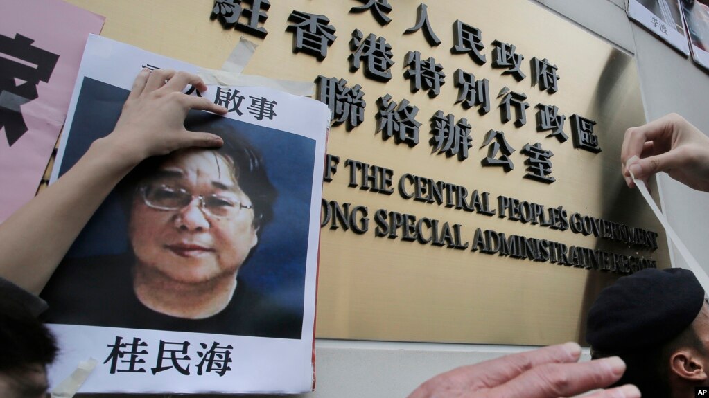 FILE - Protesters try to stick photos of missing booksellers, one of which shows Gui Minhai, at left, during a protest outside the Liaison of the Central People's Government in Hong Kong, Jan. 3, 2016. 