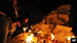 People pray near a statue in honor of quake victims during a candle rally in L'Aquila on 06 Apr, 2010, to commemorate the first anniversary of the major earthquake which struck the area