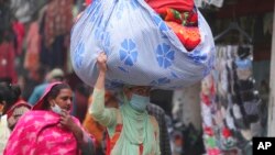 A woman wearing a face mask as a precaution against the coronavirus carries a load of blankets at a market in Jammu, India, Jan. 21, 2022.