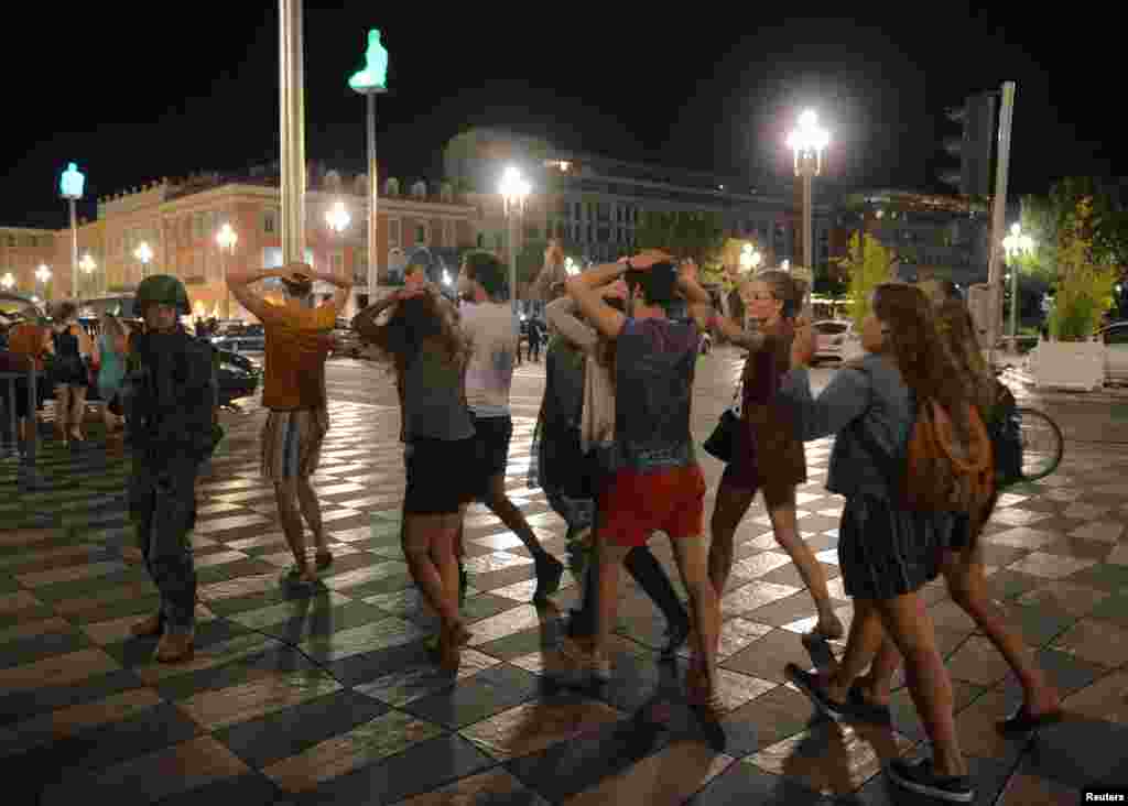 People cross the street with their hands on their heads as a French soldier secures the area July 15, 2016, after a truck ran into a crowd celebrating the Bastille Day national holiday along the Promenade des Anglais in Nice, France. 