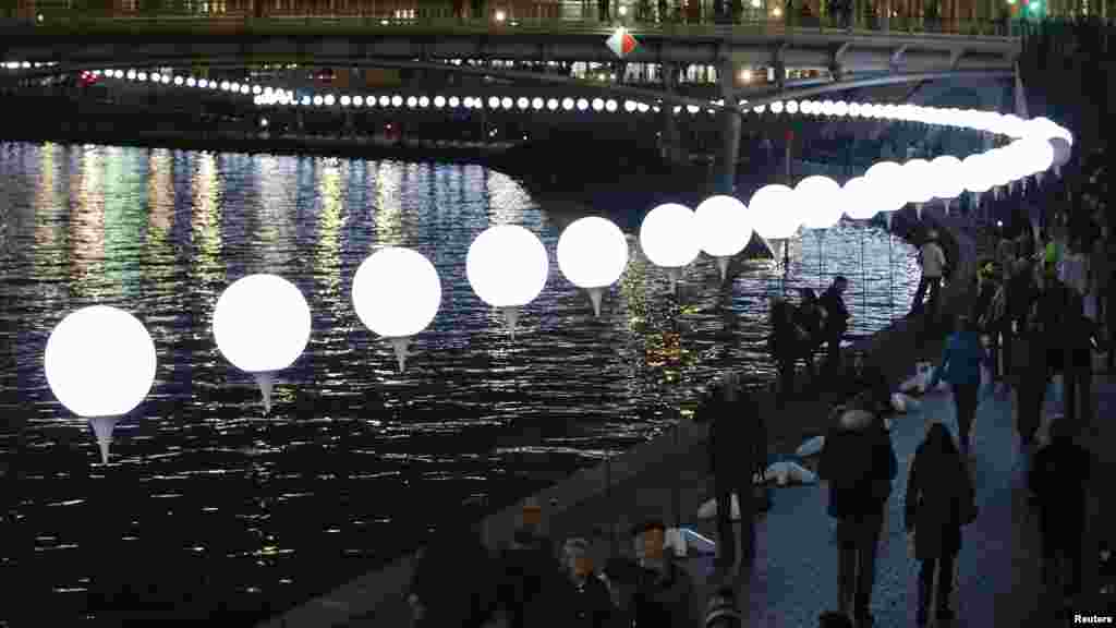 People walk under the lit balloons installation along the river Spree in Berlin, Nov. 8, 2014.