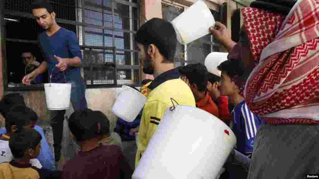 Residents carry buckets as wait for their turn to receive free meals from a soup kitchen in Raqqa, Syria.