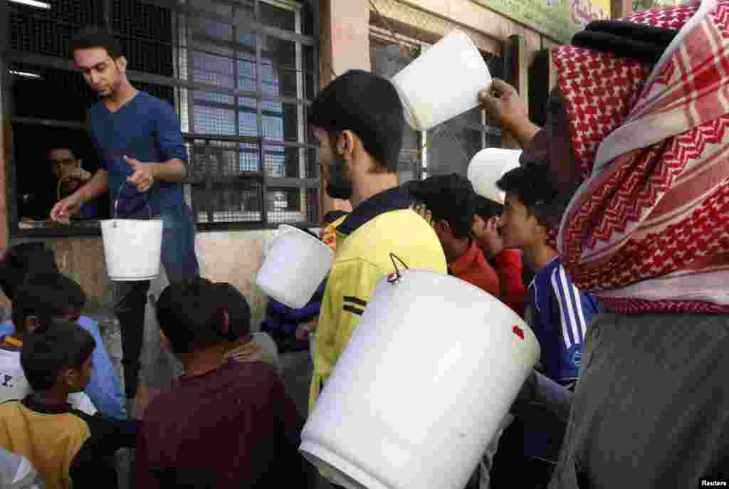 Meštani sa plastičnim kantama ulaze u humanitarni centar za dodelu hrane u Raki. 