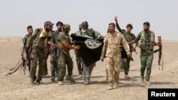 FILE - G-7 leaders are expected to discuss efforts to defeat the Islamic State. Here, Iraq's Shi'ite paramilitaries and Iraqi security forces hold an Islamist State flag pulled down in Anbar province, May 26, 2015.