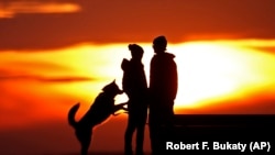 A couple pauses to take in the view of a colorful sunset while walking their dog in a park, Thursday, Jan. 28, 2016, in Portland, Maine.