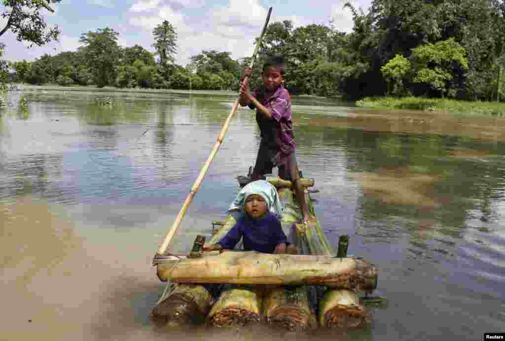 Um rapaz rema numa jangada transportando outra criança pelas áreas inundadas de Lakhimpur, no nordeste do estado indiano de Assam. Agosto 18, 2014.