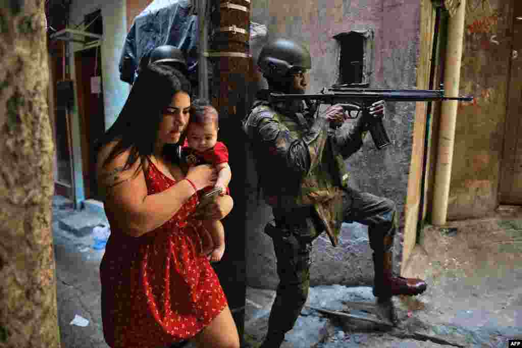 A woman walks with her baby past a militarized police soldier in position and aiming his rifle in Rocinha favela in Rio de Janeiro, Brazil, Sept. 23, 2017.