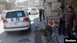 FILE - Residents watch from a sidewalk as a convoy of U.N. vehicles carrying a team of United Nations chemical weapons experts drive past, at one of the sites of an alleged chemical weapons attack in the Damascus suburbs of Zamalka, Syria, Aug. 28, 2013.